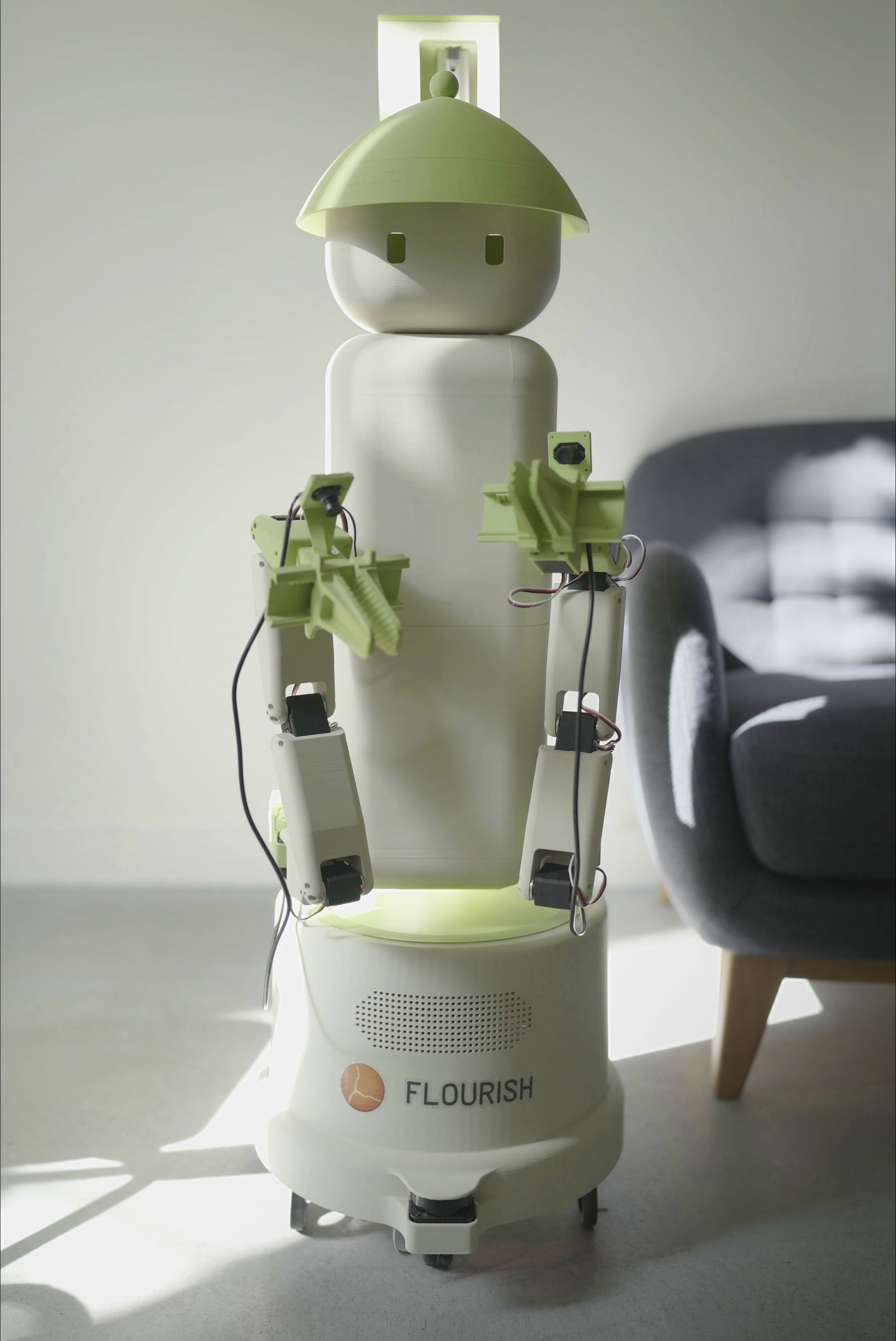 Flourish 1 wheeled home robot with green grippers and cap in a living room